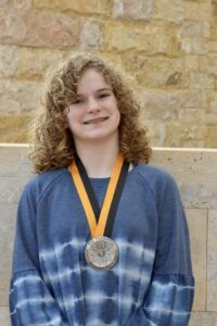 Hadley smiling in a blue shirt wearing a medal around her neck for the 2021 Prudential Spirit of Community award