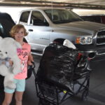 Hadley holding a large teddy bear with a wagon of stuffed toys.