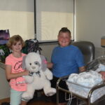 Hadley presenting a large stuffed animal to a boy and baby.