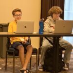 Hadley and another child sitting in front of laptops at a folding table.