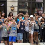 Hadley standing in a crowd of kids all making hearts with their hands.