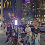 Hadley posing with a group of teenagers in New York City at night.