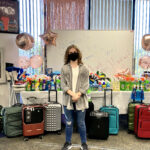 Hadley stands in front of a table full of donated supplies and luggage for the Hadley's Bags of Hope event