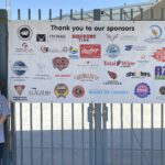 Hadley smiles in front of a sign presenting all of Hadley's Hope's sponsors.