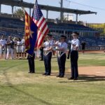 Uniformed people with flags and rifle on baseball field.