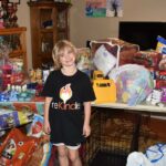 Hadley smiling in front of large table full of donated pet supplies.