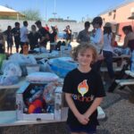 Hadley standing in front of picnic tables full of donations.