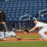 Baseball player catches a ball while a player slides into base on their chest.