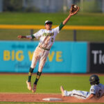 Baseball player from the Peoria Panthers jumping up to catch a ball while a player slides into the base.