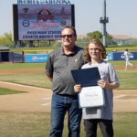 Hadley being presented with a certificate on a baseball field.